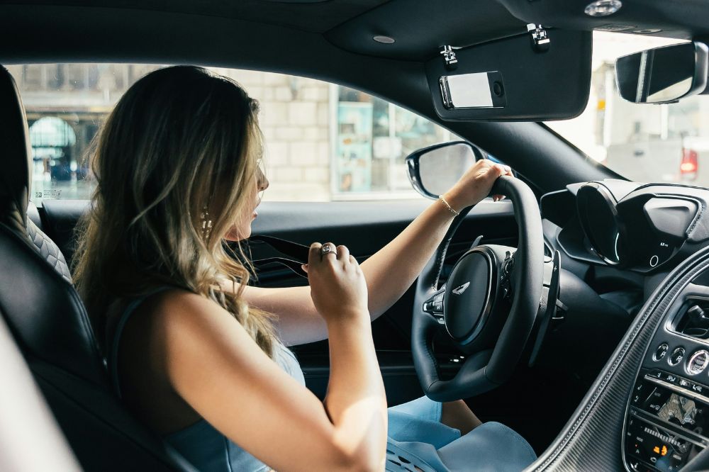 Eine Frau sitzt am Steuer ihres Autos und ruft die HUK-Autowelt an, wenn sie Fragen hat.