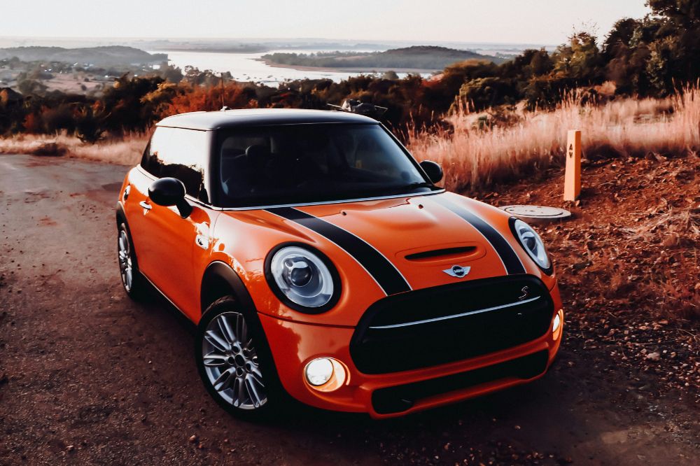 Ein roter MINI Cooper der deutschen Automarke steht am Straßenrand einer Altstadt. 